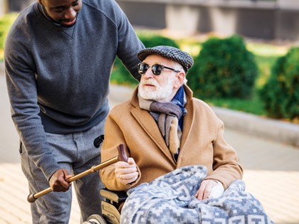 A man talking to another man while pushing him in a wheelchair