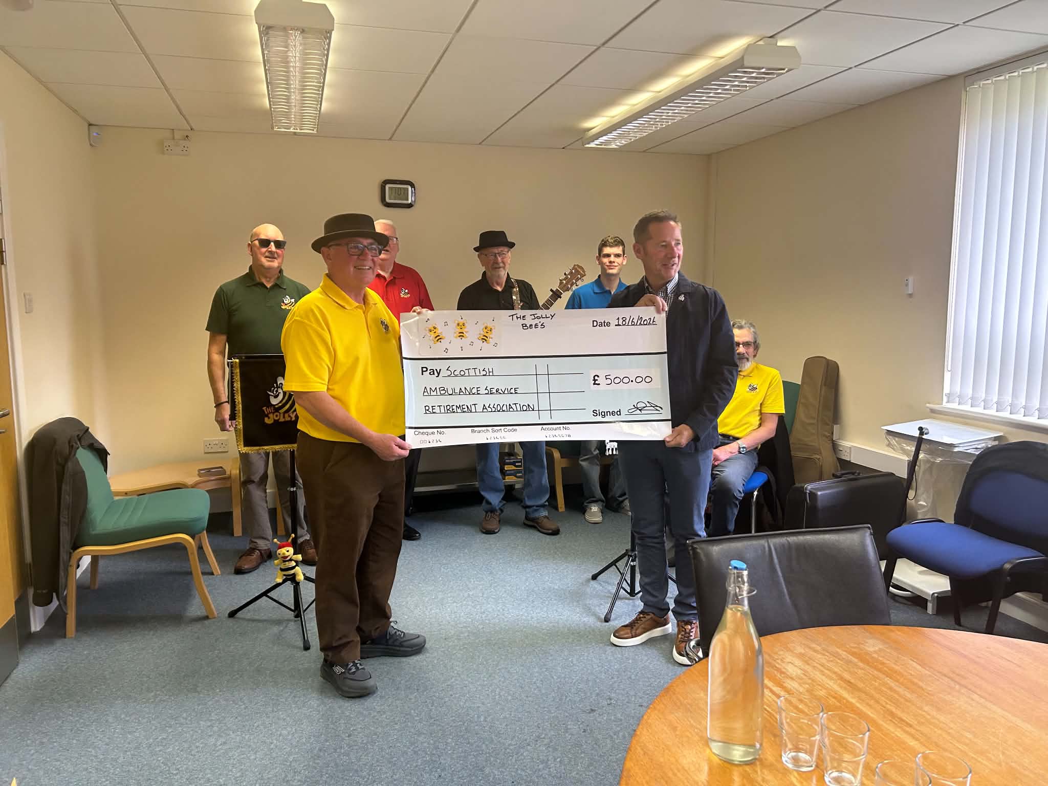 Group of men from Jolly Bees singing group in a room presenting a large check for £500 to SASRA.