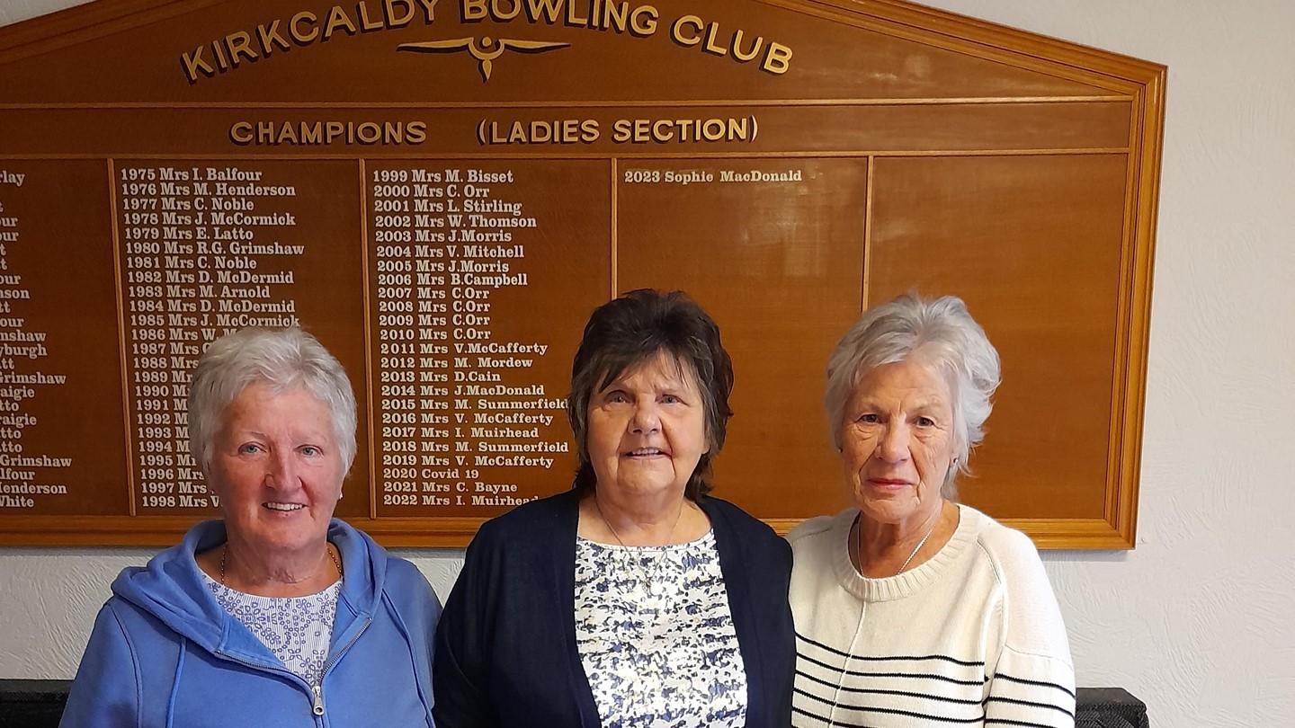 Three women standing in front of Kirkcaldy Bowling Clubs indoor sign.