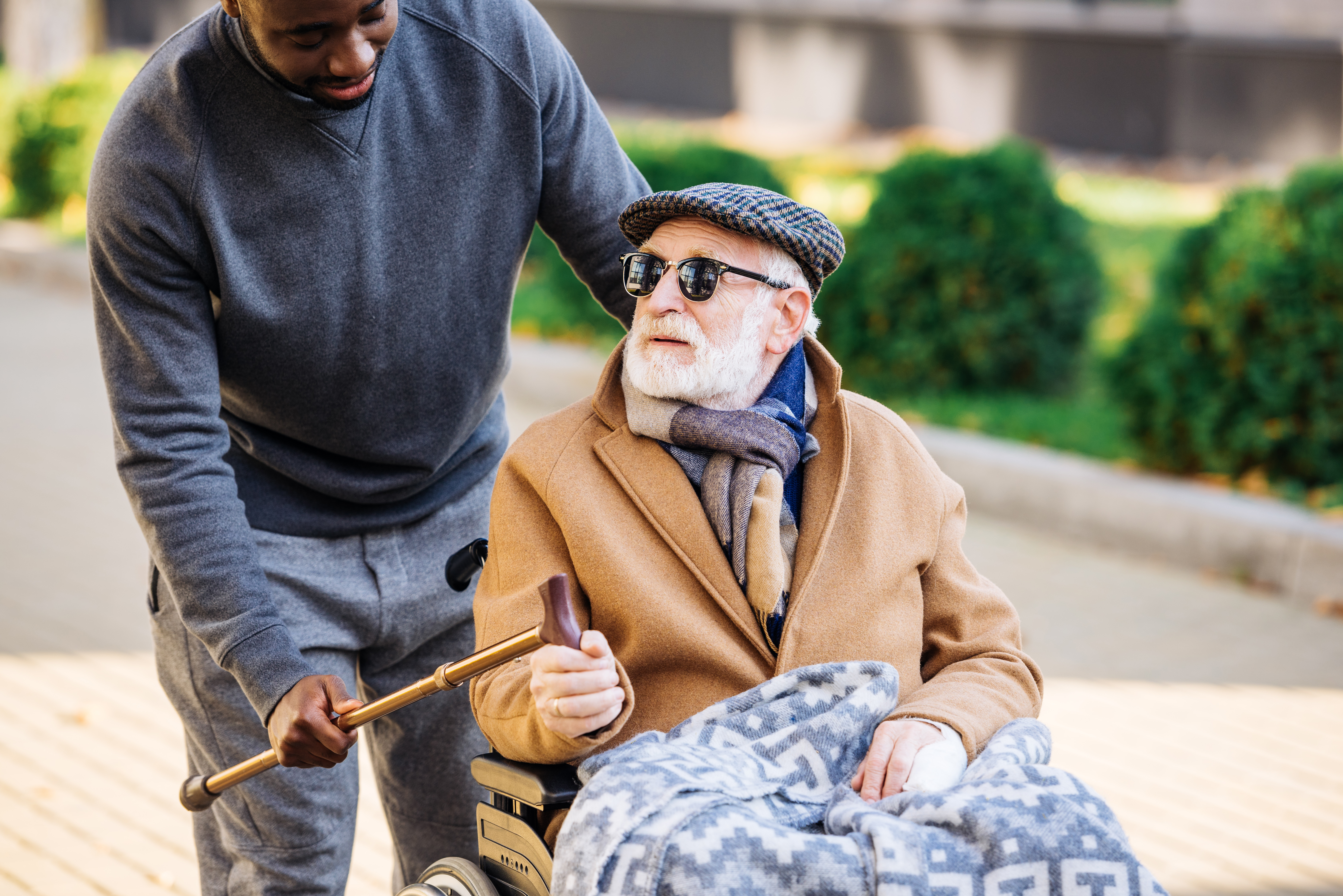 A man talking to another man while pushing him in a wheelchair