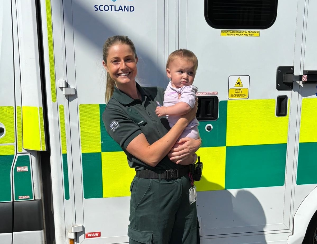 Paramedic Nicola McGregor holding Baby Phoenix standing in front of a parked ambulance.