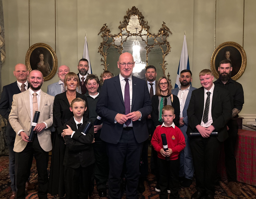 First Minister John Swinney stands in the centre surrounded by all the other Brave@Heart winners proud in a group shot