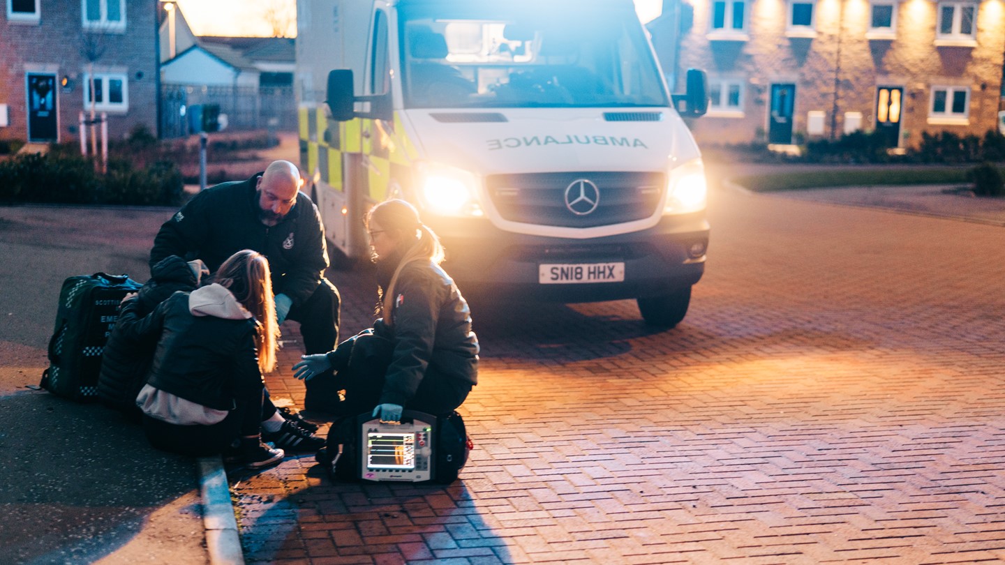 A crew treat a patient at the side of the road with the ambulance behind