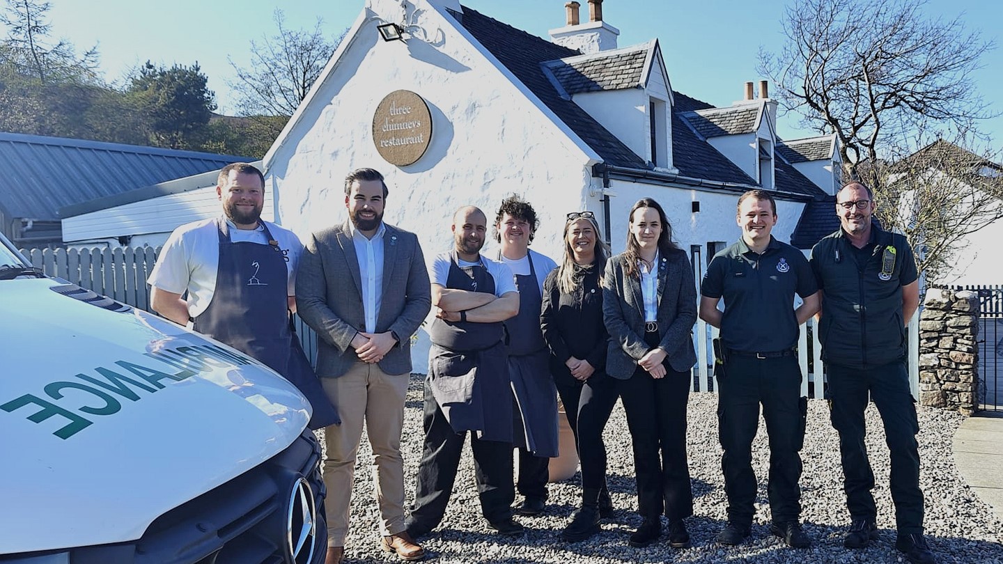Restaurant staff stand together with Scottish Ambulance Service staff smiling in front of Three Chimneys with an ambulance in the foreground