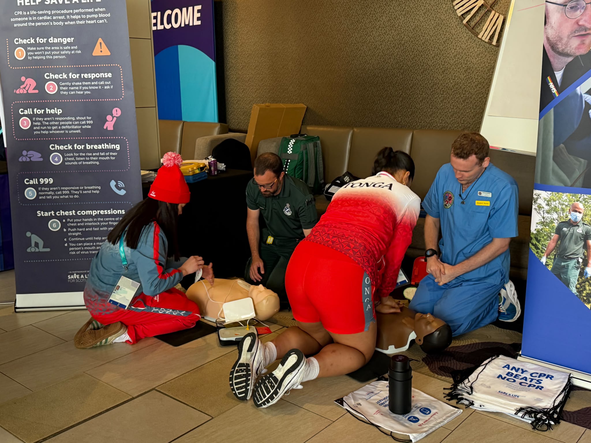 Two medical professionals instructing two athletes from Tonga on how to perform CPR in a training session.