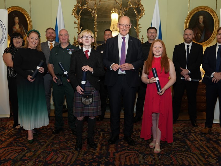 A group of 12 people dressed in black tie attire holding their awards.