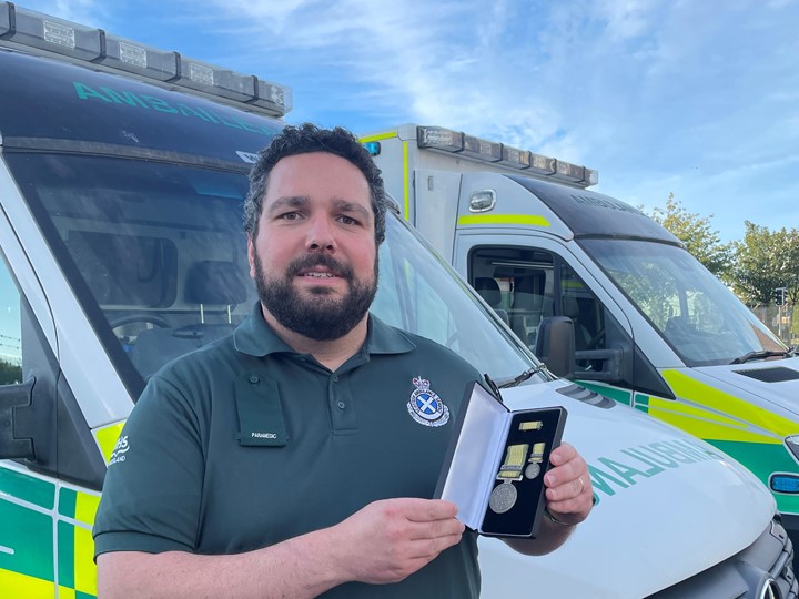 Paramedic Steve holding his medal in front of an ambulance