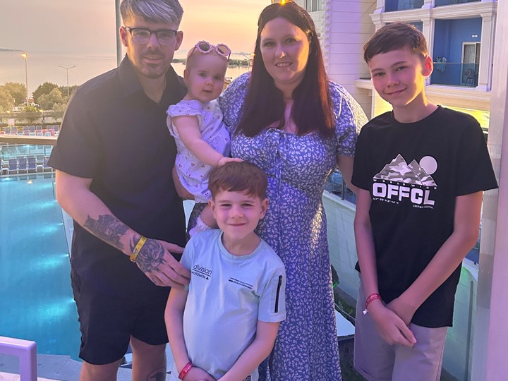 Shannon and her entire family pose for a photo on a holiday. Kids and husband look towards camera with the sun setting in the background