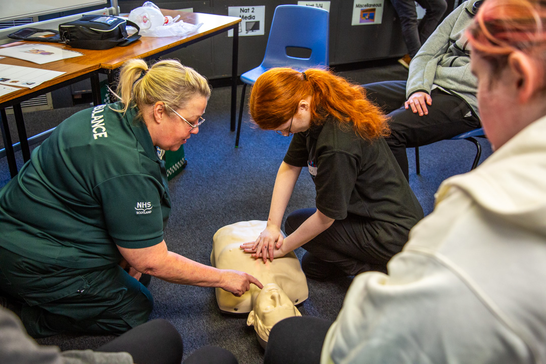 A Paramedic shows a school pupil how to perform CPR on a mannequin