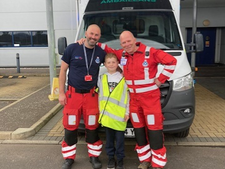 SAS staff members dr Davis and Steven McIntosh smile with Calon in the centre, with an ambulance vehicle in the background