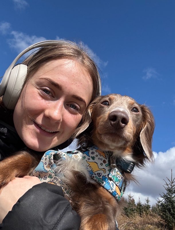 Nicole Ross smiles with her dog with a bright blue sky in the background