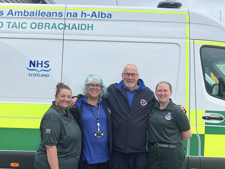 Sam Grieve, Mary and John Kinninmonth, and Laura Cameron standing together, smiling, in front of a parked ambulance vehicle