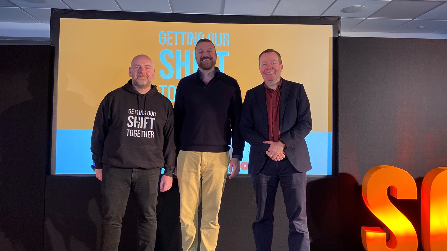 Three men stood on the stage smile at the camera at the Scottish Cardiac Arrest Symposium 2023