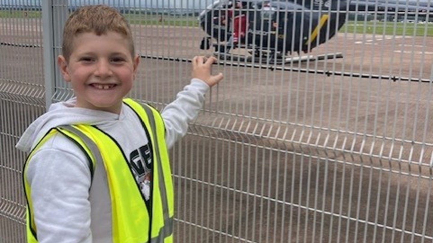 Calon, with a big smile on his face, looks out through a fence at a helicopter