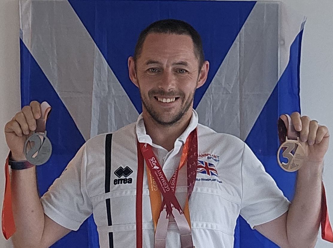 Frank in his running gear proudly holds two of his medals smiling