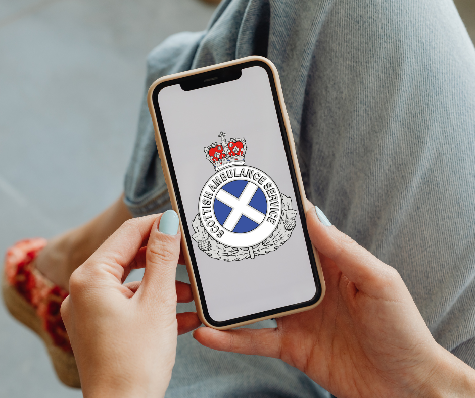 Person holding a smartphone displaying the Scottish Ambulance Service logo with a crown and blue saltire cross.