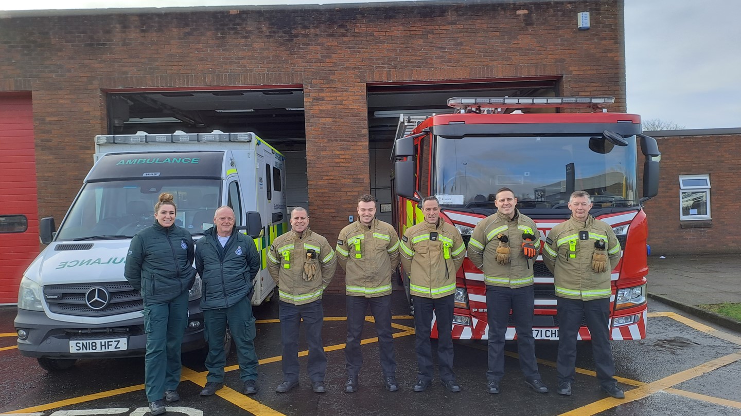 Ambulance staff with Scottish Fire and Rescue staff stand in front of an ambulance and Fire Engine at a station