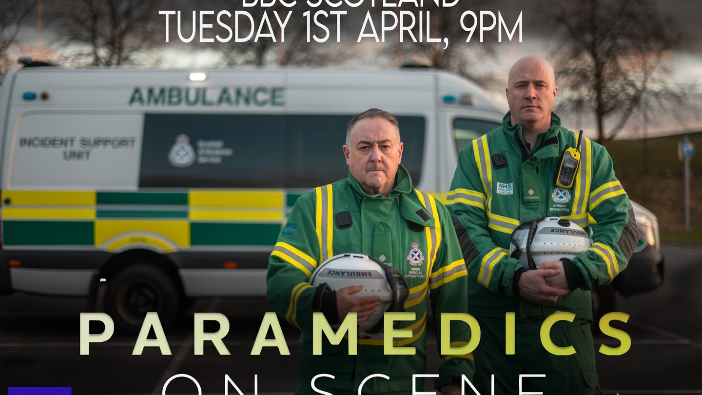 Two SORT members of staff stand proudly with their helmets with the title card of the show highlighted in front