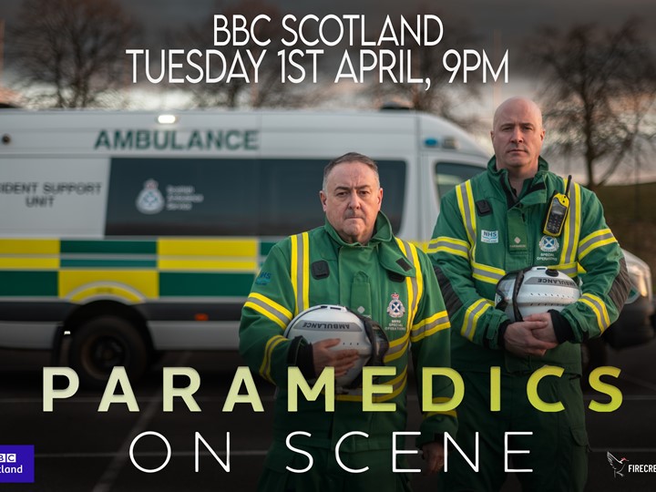 Two SORT members of staff stand proudly with their helmets with the title card of the show highlighted in front