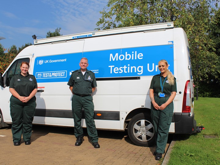Three members of staff in front of a mobile testing unit