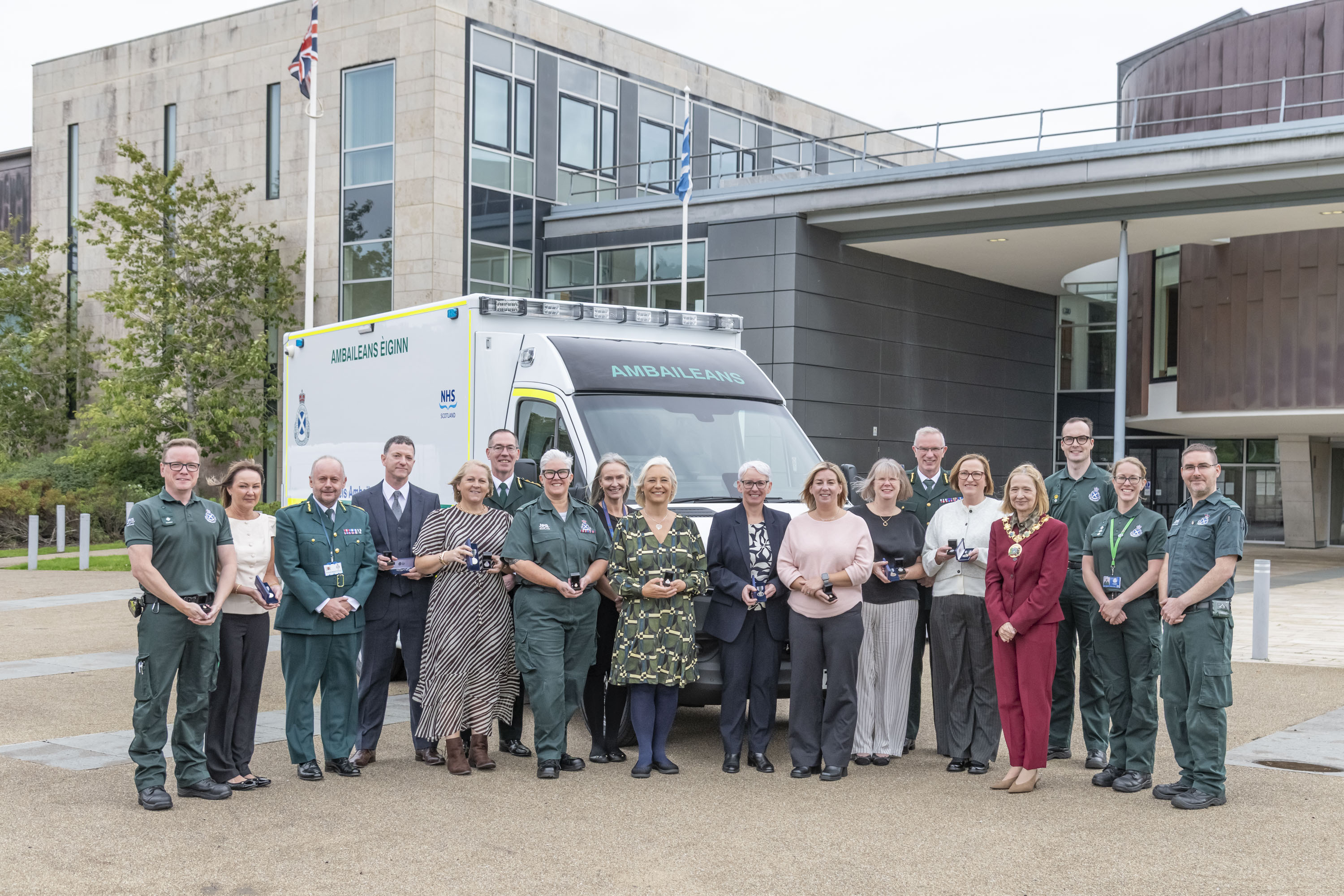 Group shot of staff receiving their medals with members of the council with an ambulance in background