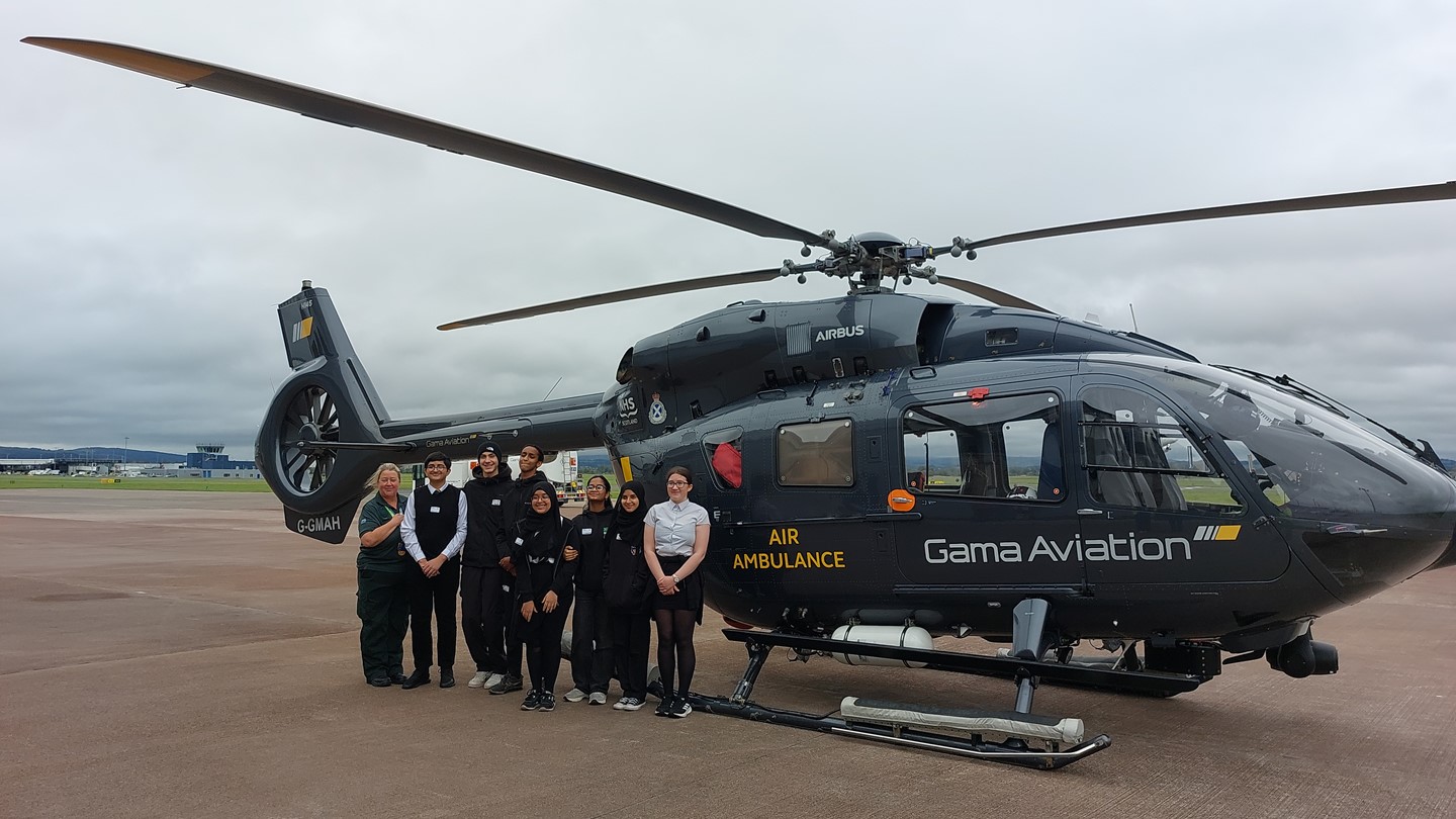 Group of school children and a paramedic standing in front of an air ambulance at Glasgow Airport