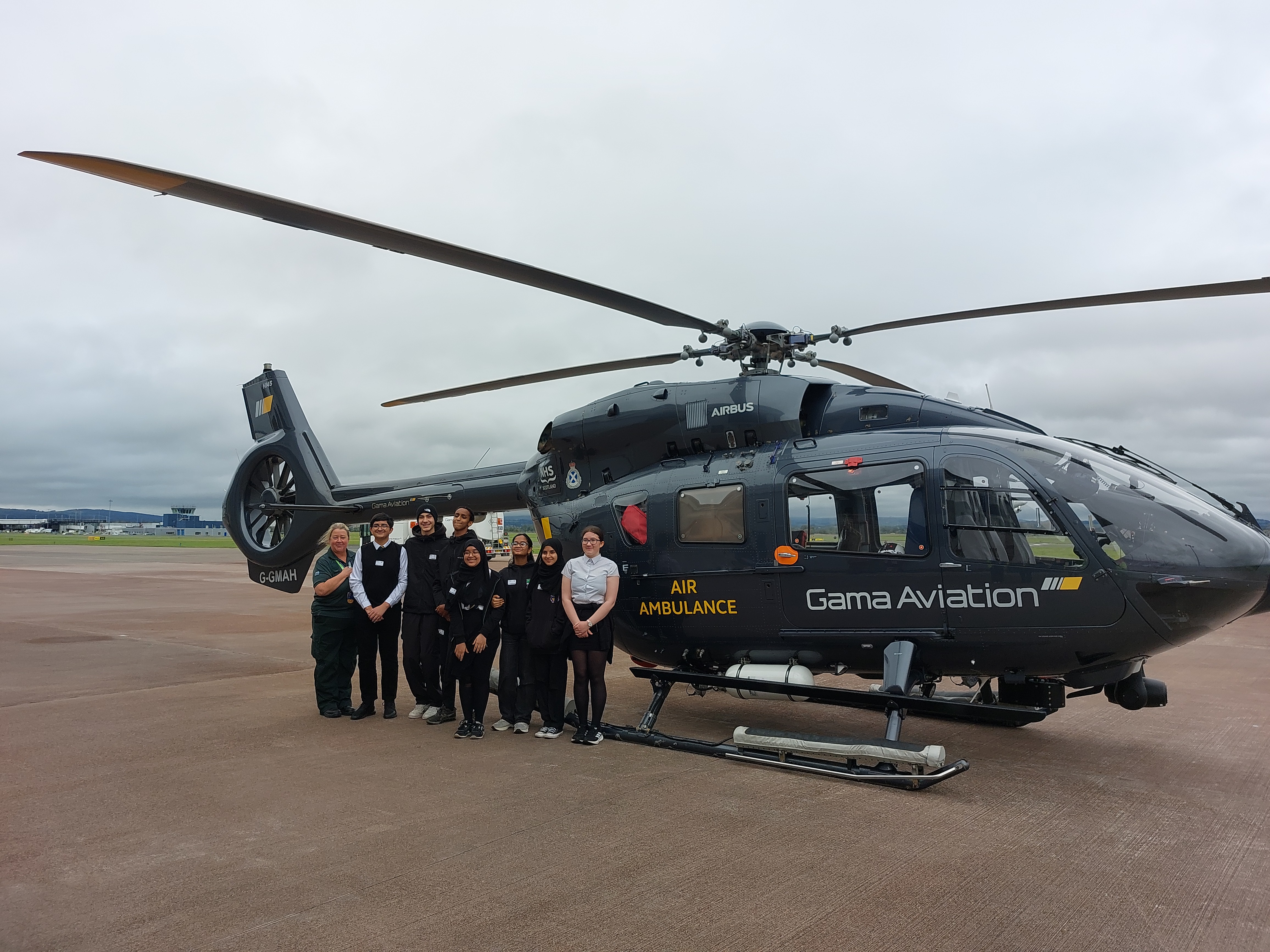 Group of school children and a paramedic standing in front of an air ambulance at Glasgow Airport