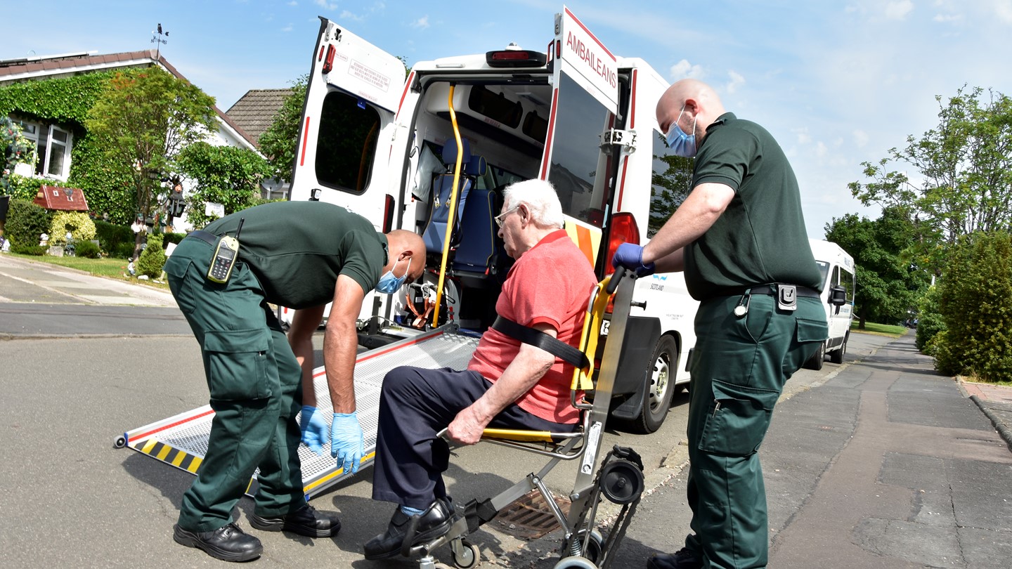 Two Ambulance Care Assistants help a patient onto an ambulance