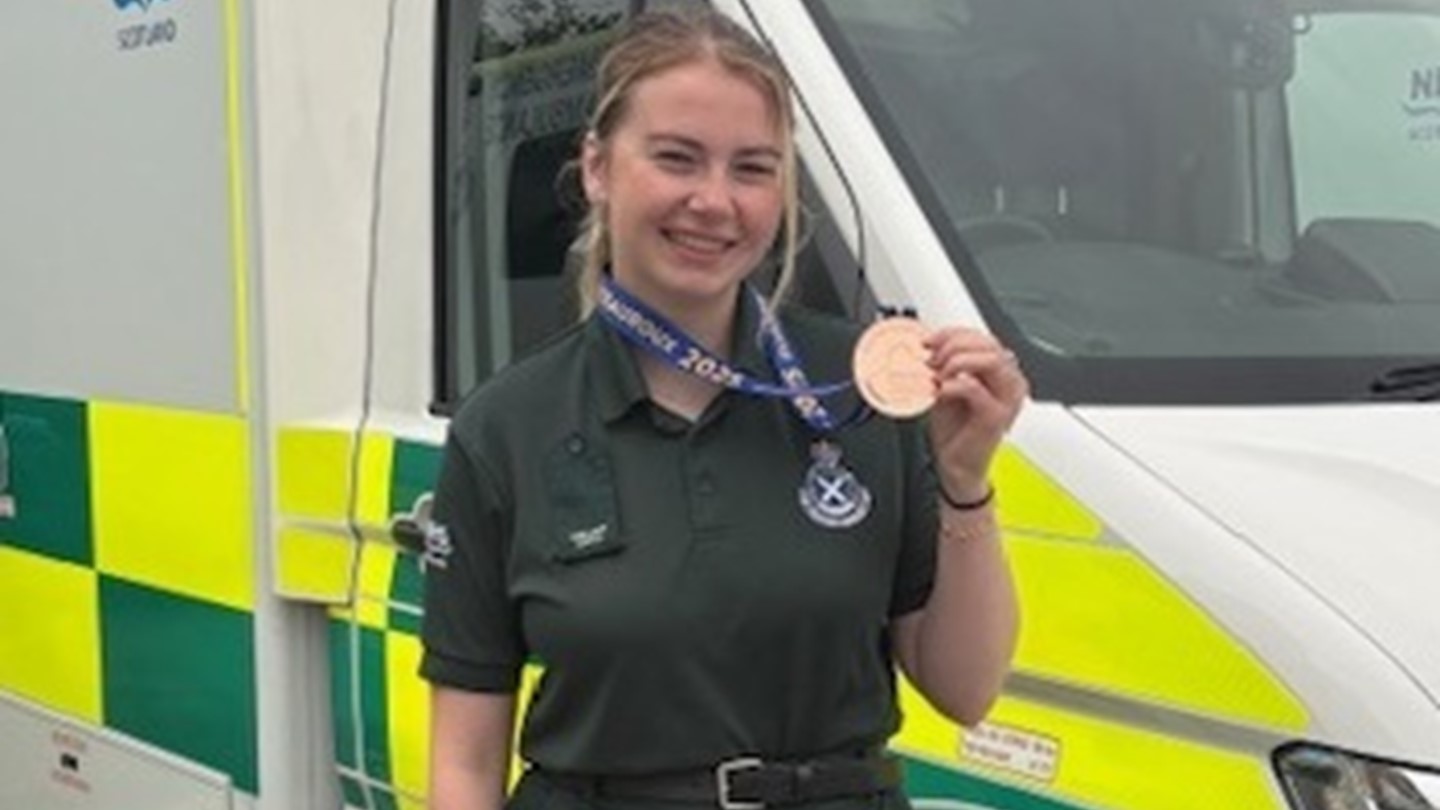 Izzy proudly displays her medal standing in front of an ambulance vehicle