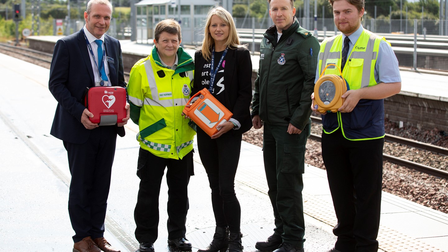 Five people with a public access defibrillator on a railway platform