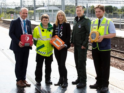Five people with a public access defibrillator on a railway platform