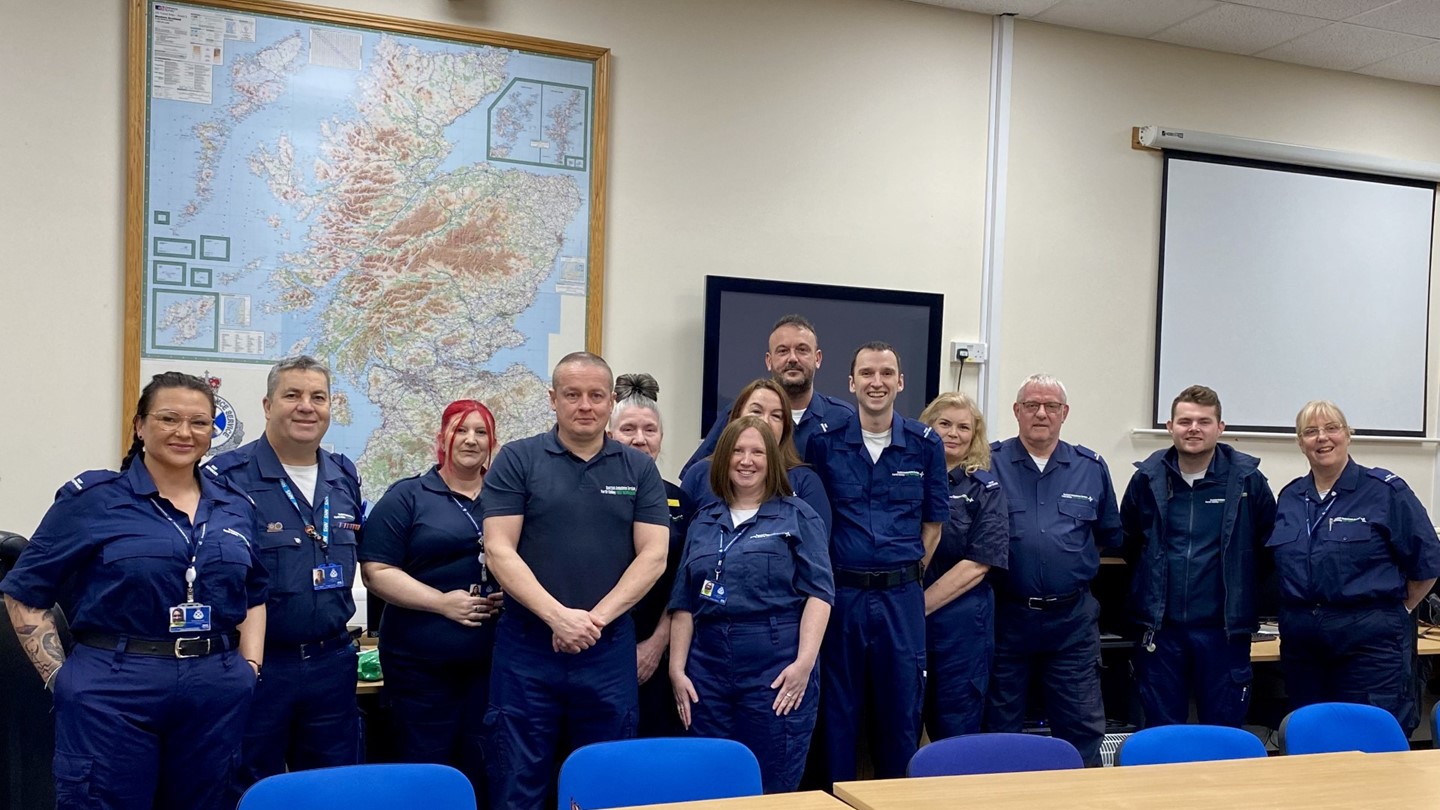 Group of 13 community first responders dressed in dark blue jumpsuits.
