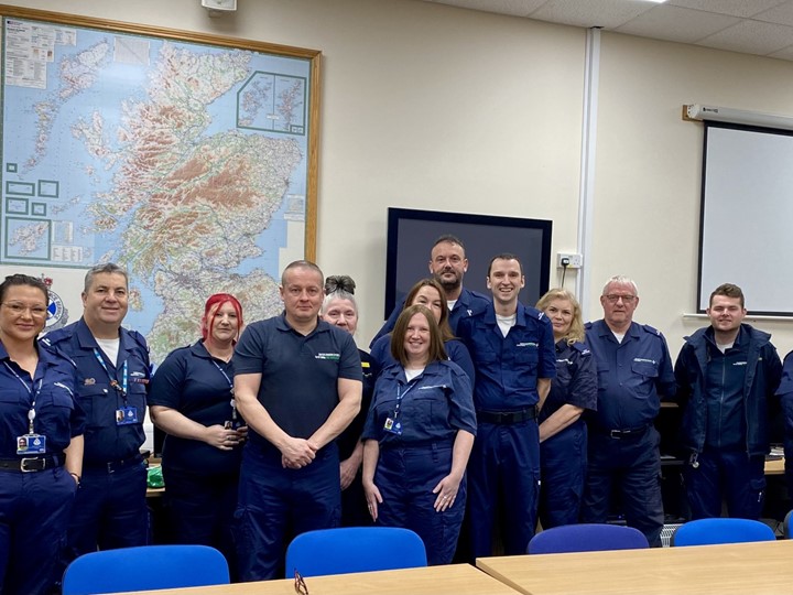 Group of 13 community first responders dressed in dark blue jumpsuits.