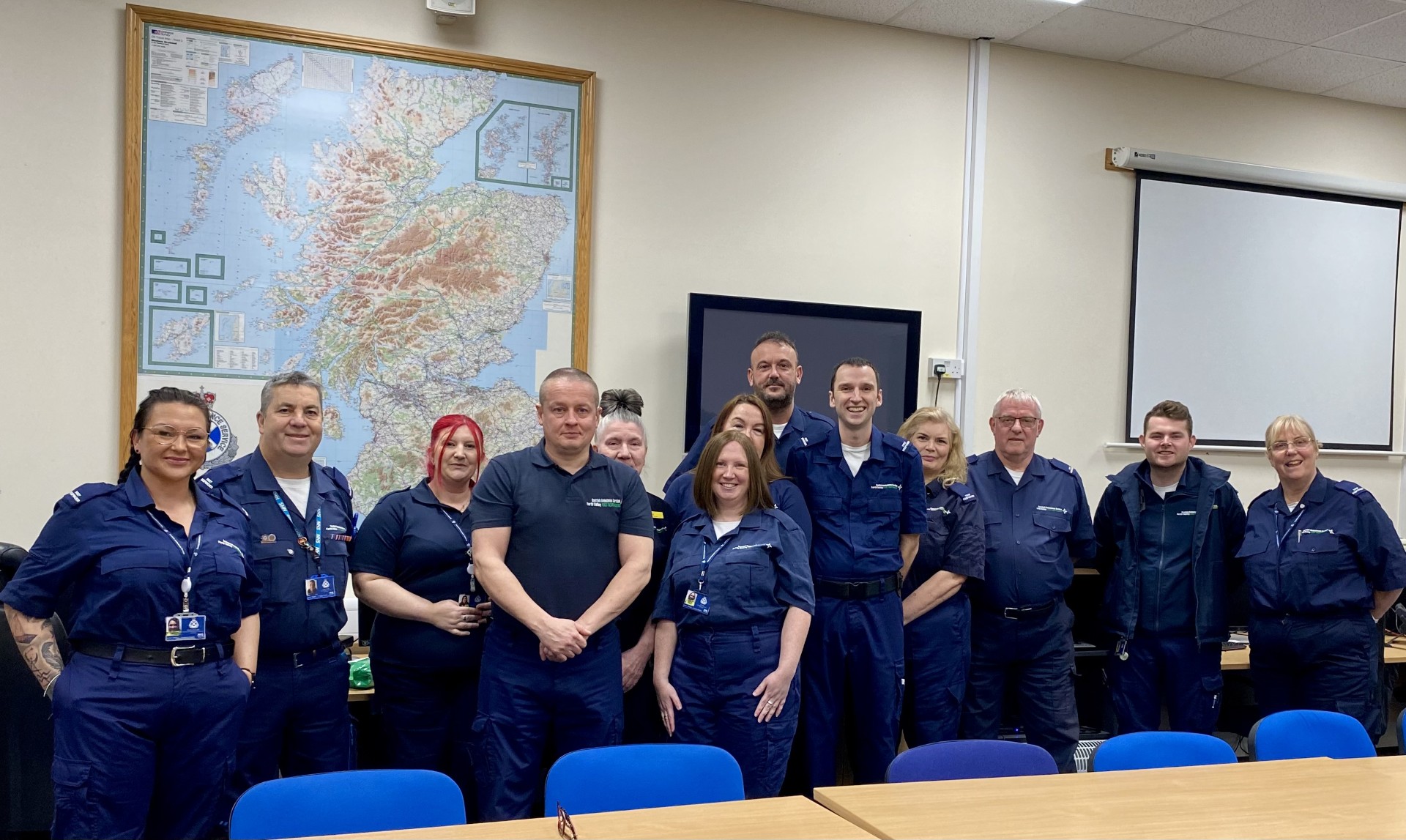 Group of 13 community first responders dressed in dark blue jumpsuits.