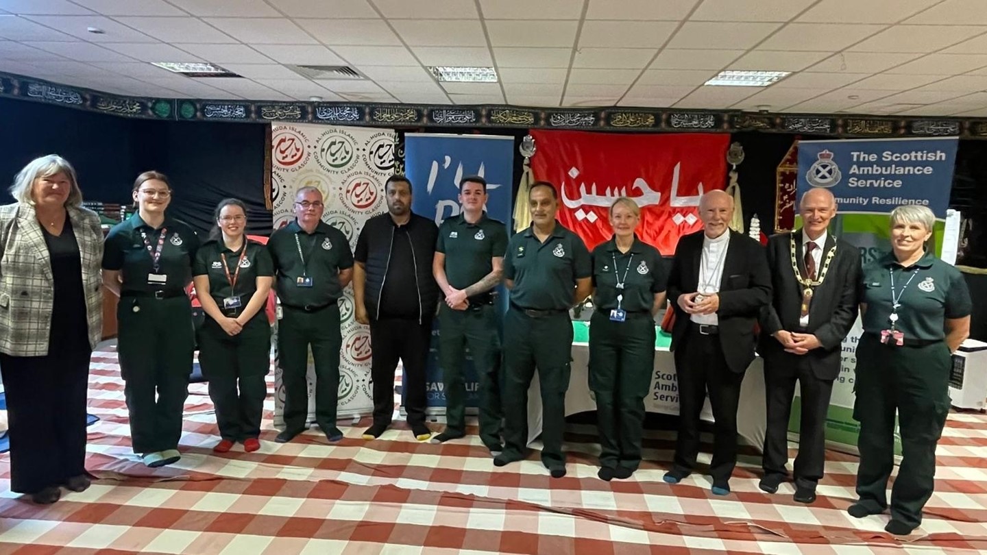 Scottish Ambulance staff and members of the public stand in front of advertising boards