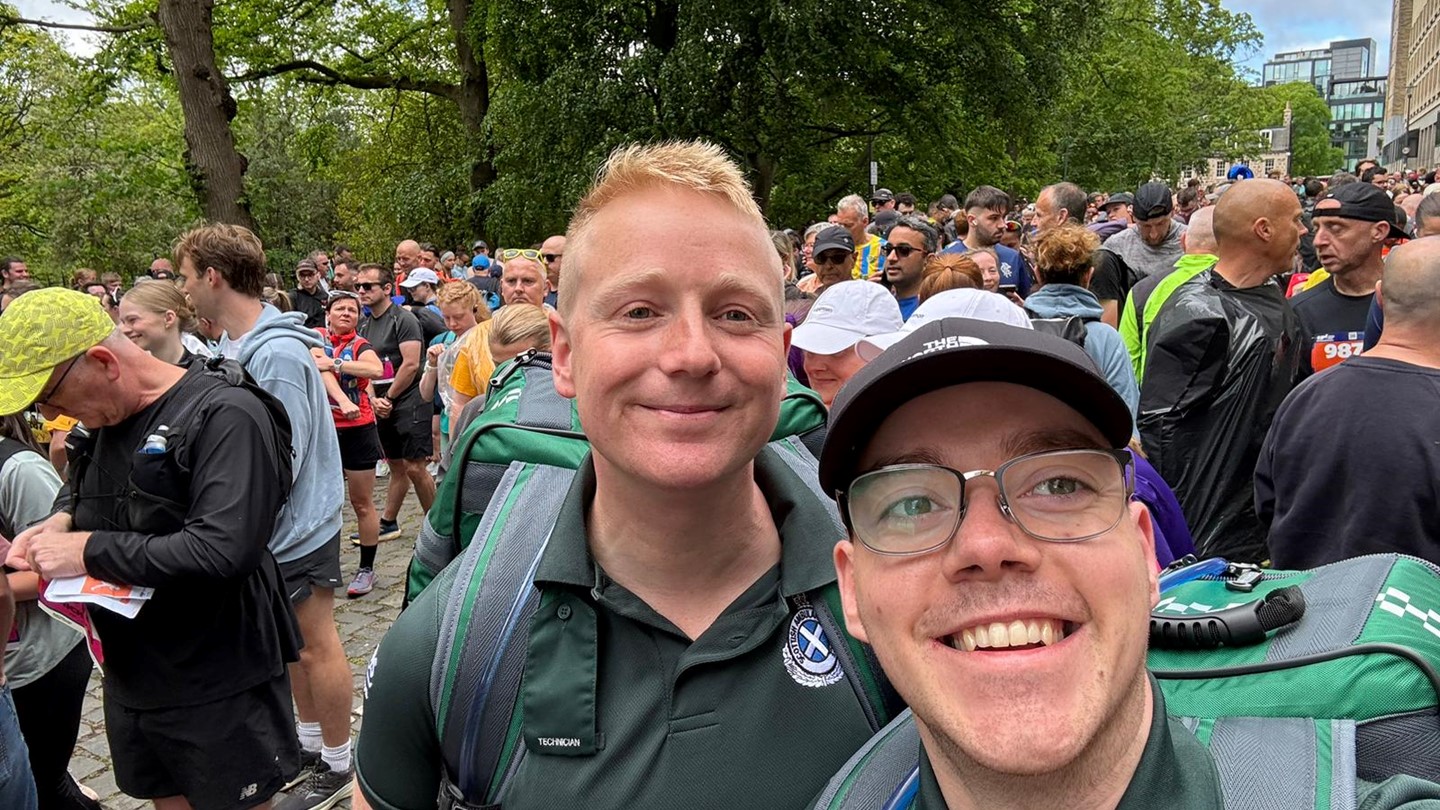 Jack and Dominic take a smiling selfie at the marathon with crowds behind them