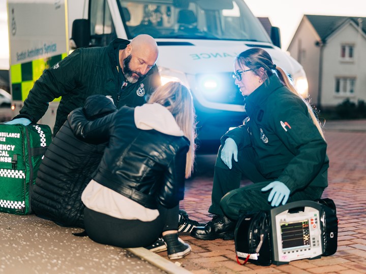 A crew treat a patient at the side of the road with the ambulance behind