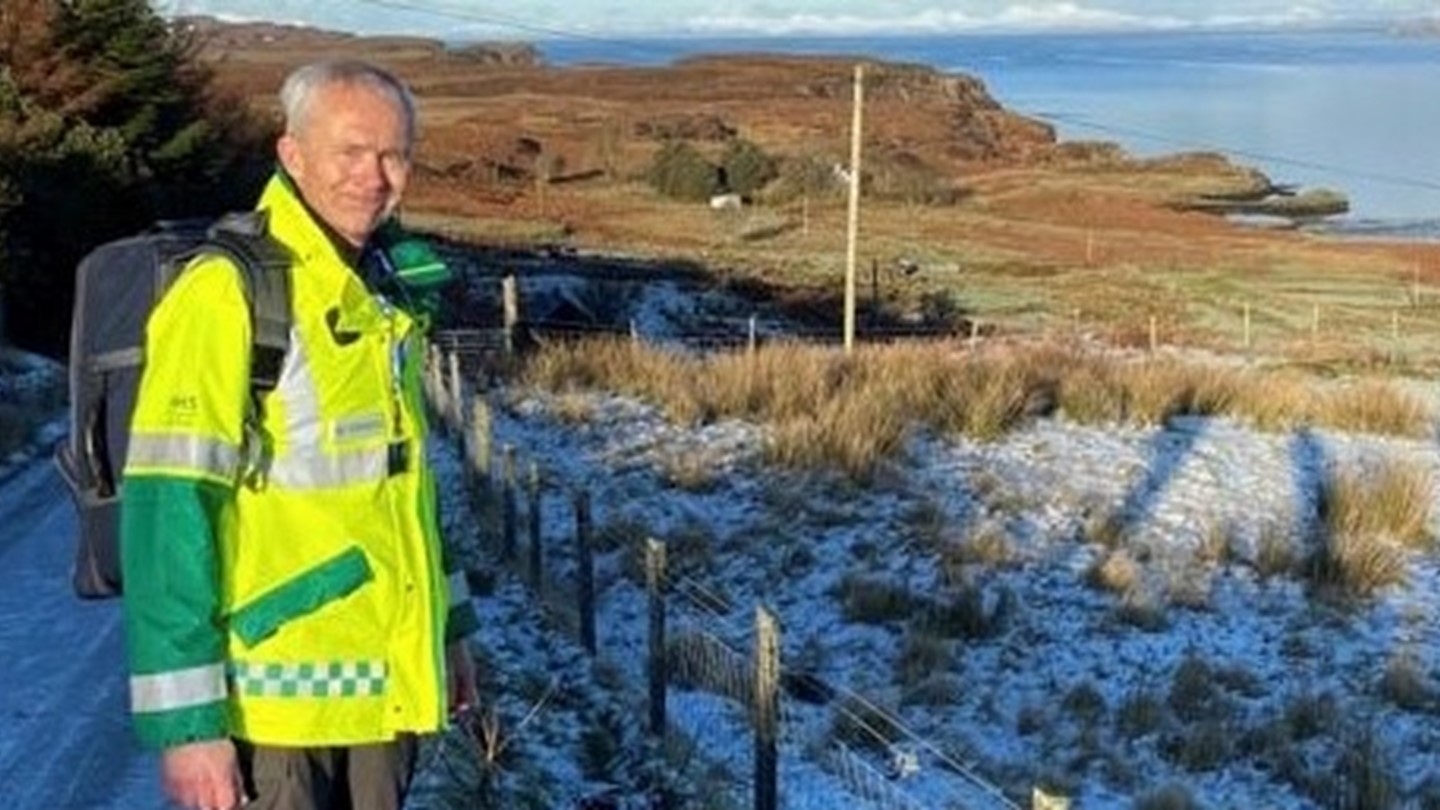 Skye volunteer Steve Brealey dressed in high vis jacket standing on a snow covered road.