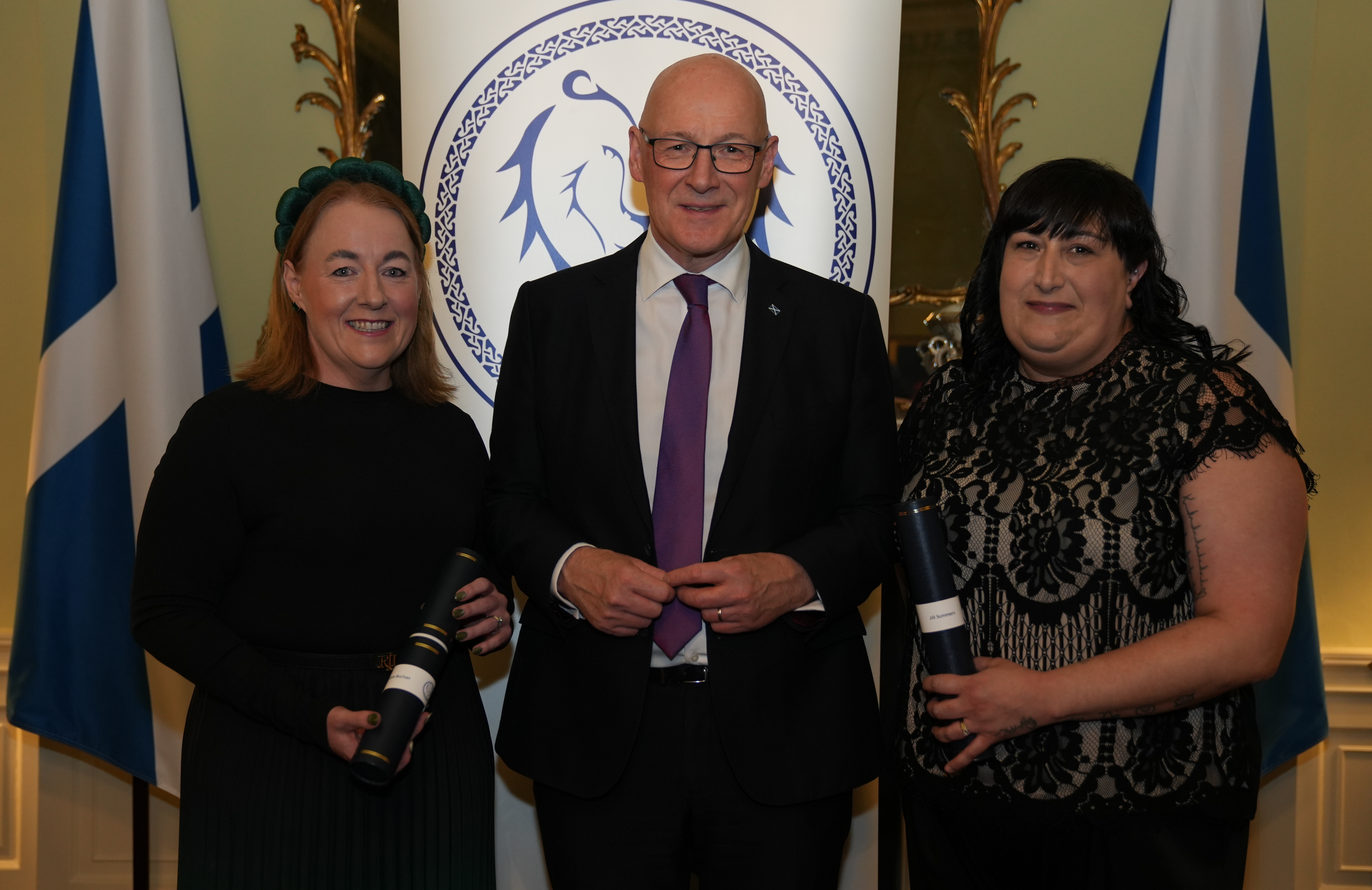Jill Summers and Colene Buchan holding their awards stood with John Swinney. All dressed in black tie attire.