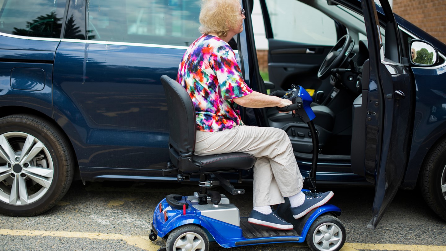 A lady in a mobility scooter about to get into a car