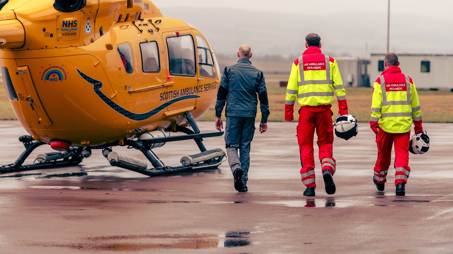 Three members of a helicopter crew walk towards the helicopter on the tarmac