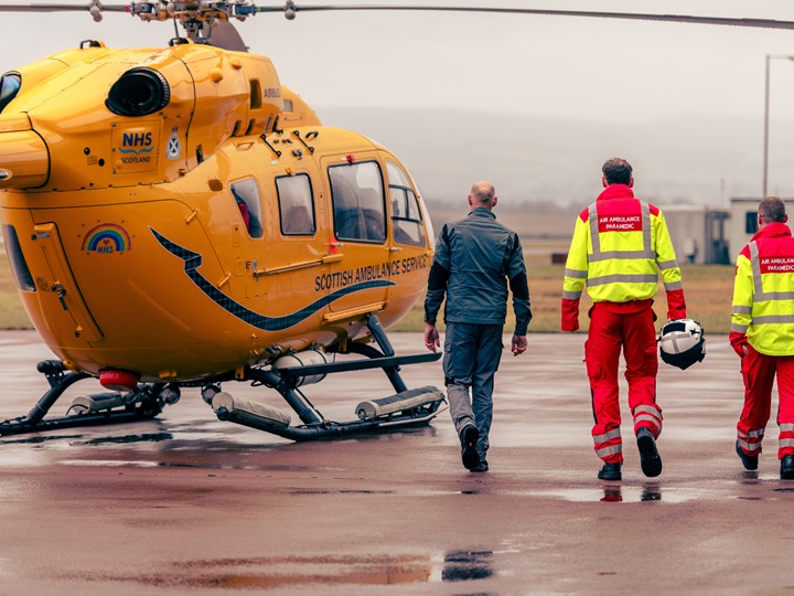 Three members of a helicopter crew walk towards the helicopter on the tarmac