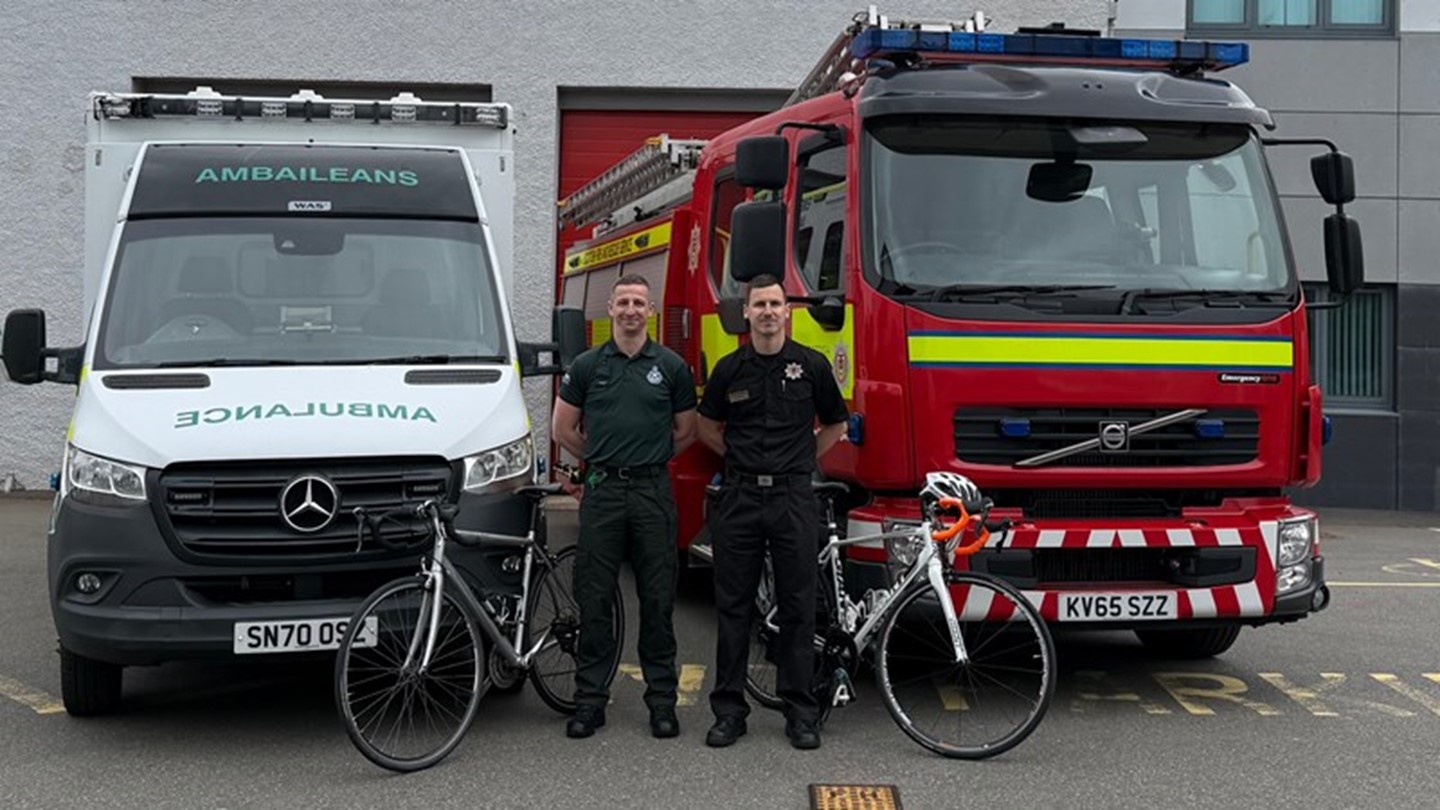 Paramedic Christopher and his firefighter brother John stand proudly in front of an ambulance and fire truck with bikes near them